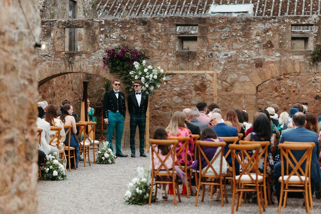 groom + best man standing next to floral arch