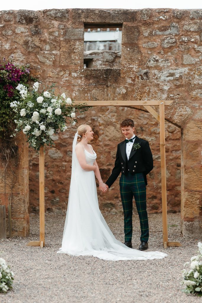 bride + groom standing in front of floral arch
