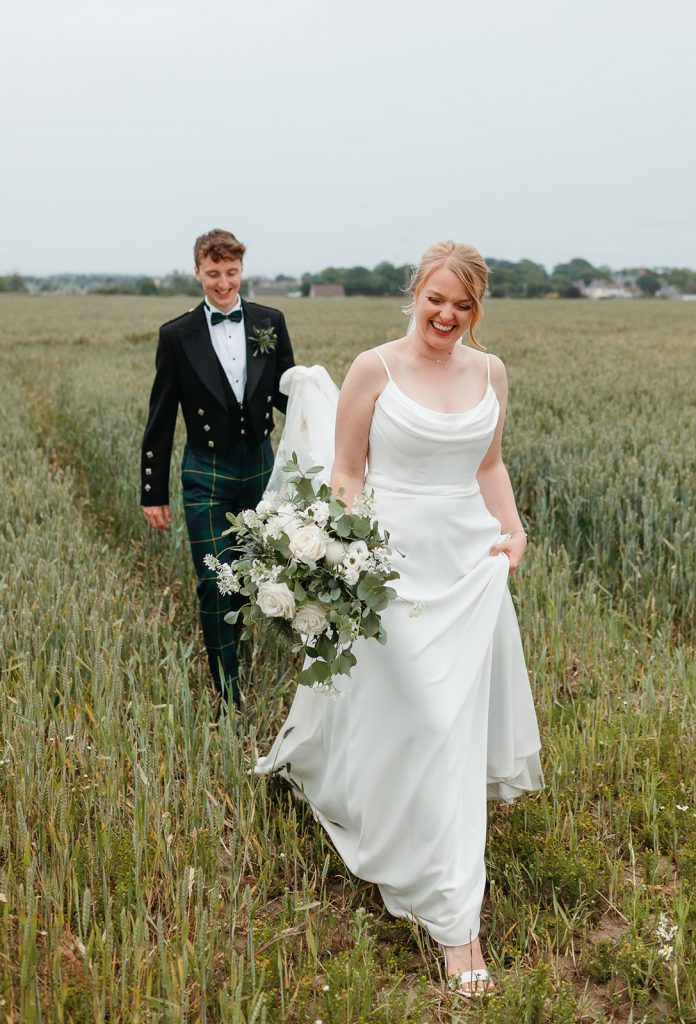 bride carrying bouquet walking with groom in a field