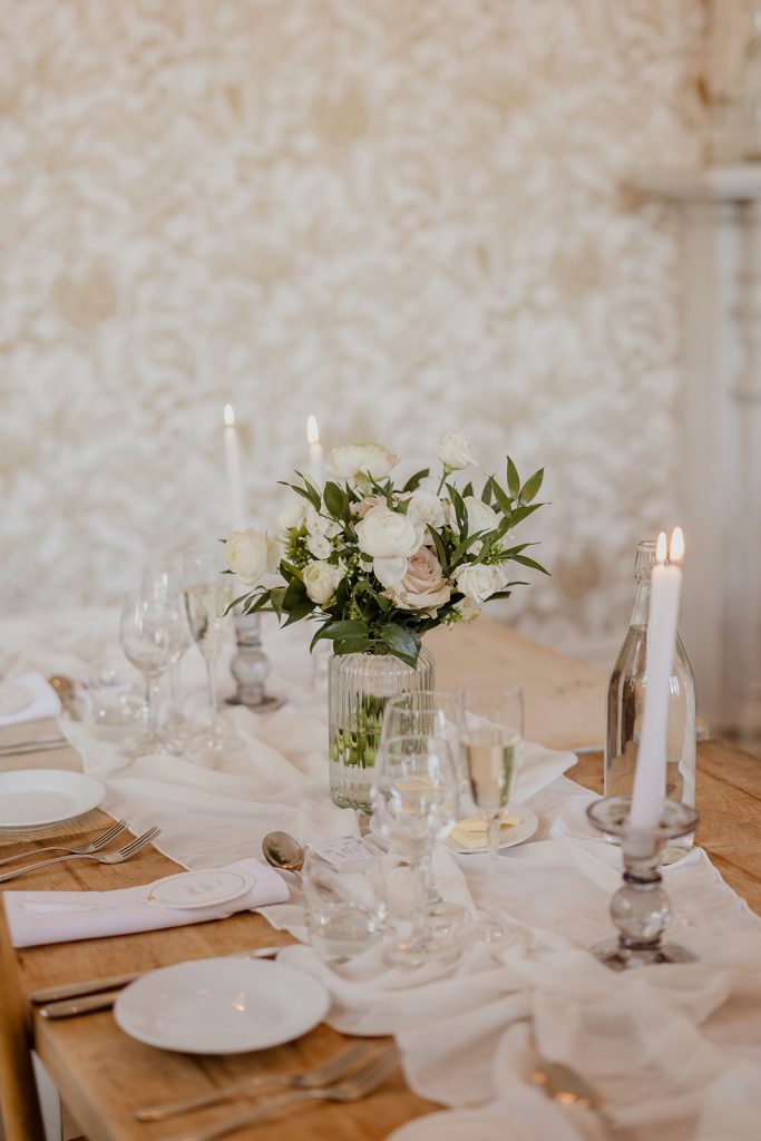 Elegant dining table with a white floral centerpiece in a glass vase, candles, and fine place settings on a wooden table