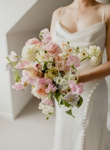Bride in a white dress holding a pastel bouquet of pink and white roses, peonies, and lisianthus.