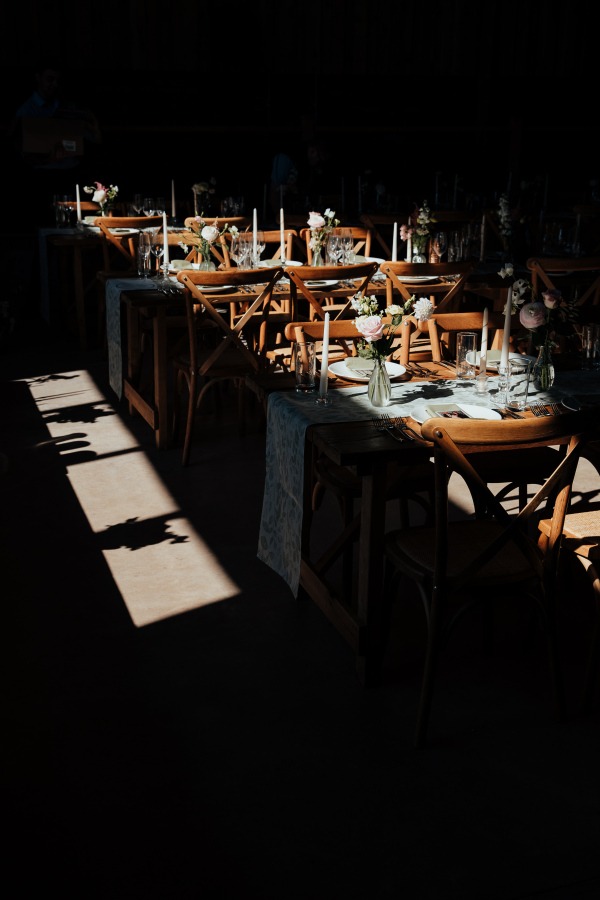 Rossie-on-the-earn-perthshire-wedding-fraoch-floral-design 18 - Fraoch Floral Design Dimly lit banquet hall with long wooden tables, floral centerpieces, candles, and chairs set for a formal event