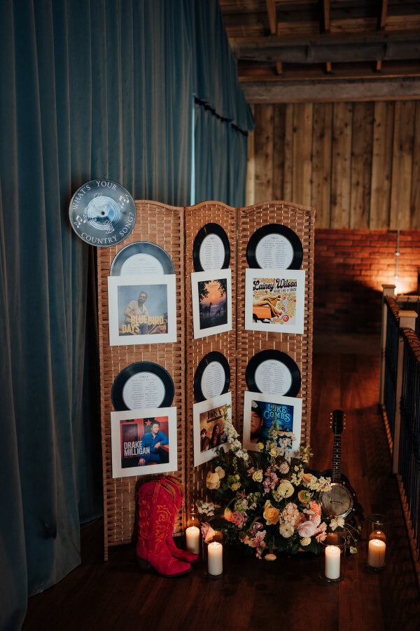 Rossie-on-the-earn-perthshire-wedding-fraoch-floral-design 21 - Fraoch Floral Design Memorial tribute display with a folding screen holding vinyl records and photos, surrounded by flowers, candles, a pink cowboy boot, and a guitar in a wooden room.