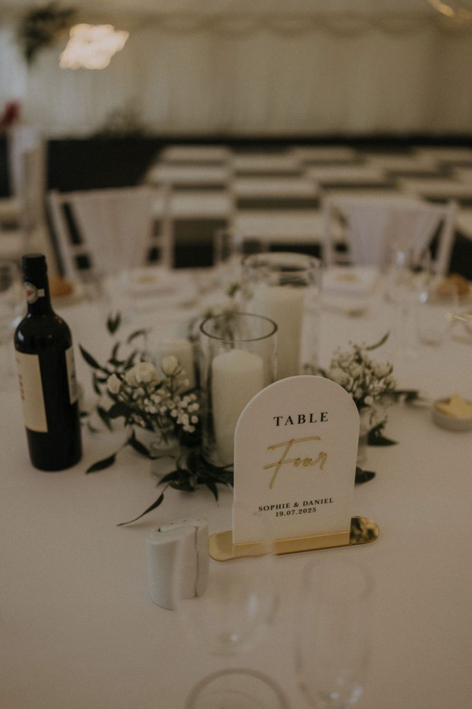 angus-wedding-florist-kinnettles-castle 5 - Fraoch Floral Design Wedding reception table with a white place card reading 'TABLE Four' beside candles and white florals.