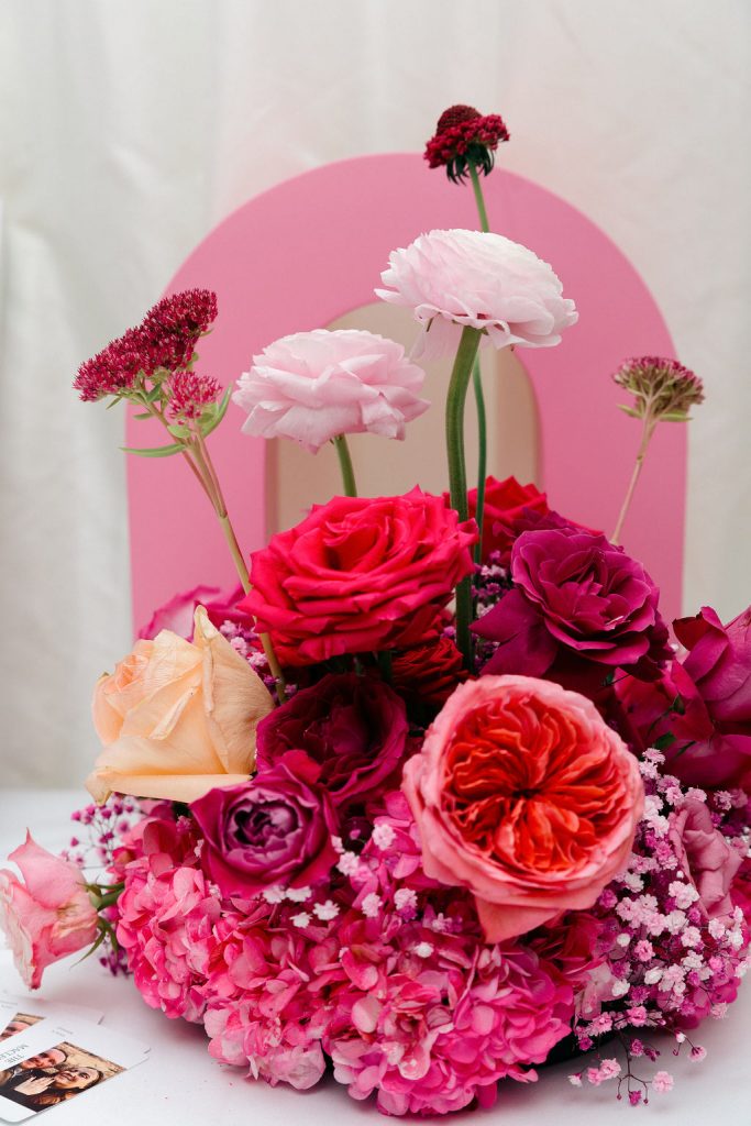 Vibrant pink flower bouquet with roses, peonies, and baby's breath on a light table, against a pink backdrop.