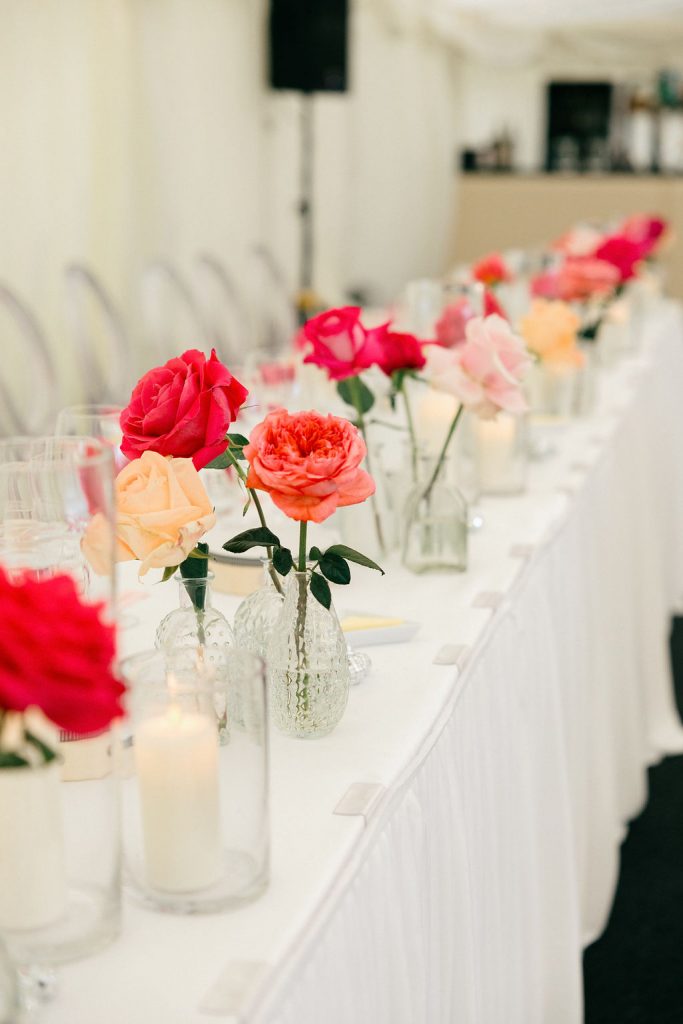 angus-wedding-flowers-florist-fraoch-floral-design 22 - Fraoch Floral Design Banquet table with pink, red, and peach roses in clear glass vases, candles, and white linens.