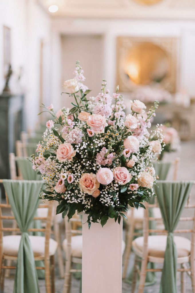 Blush pink rose centerpiece with baby's breath on a white pedestal at an elegant event venue.