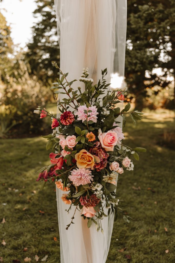 Floral arrangement with pink, peach, and white blooms wrapped around a white fabric post outdoors.