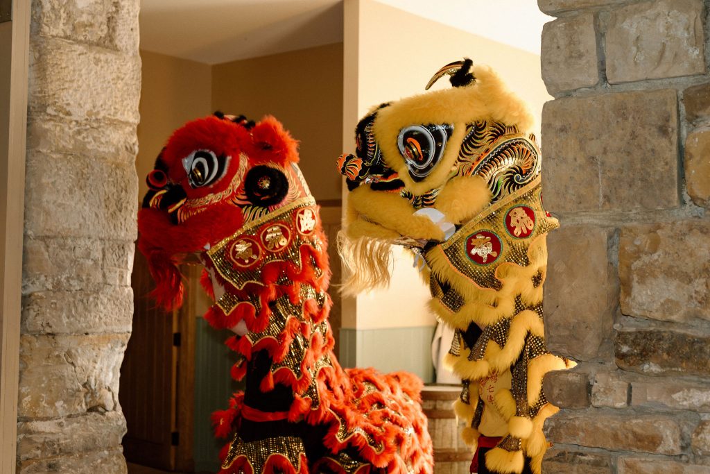 Two ornate lion dance costumes, yellow and red, peeking through a doorway between stone walls.