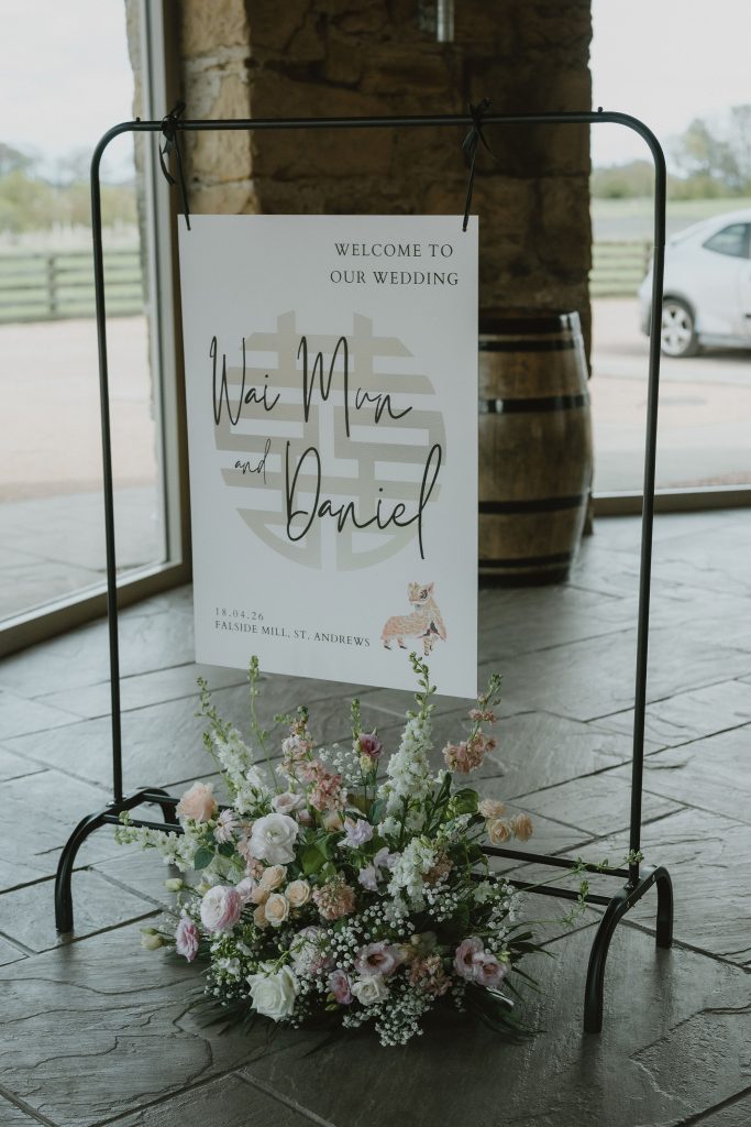 Wedding sign on a black metal frame with a flower-adorned base; reads'Welcome to our wedding' for Wai Min and Daniel.