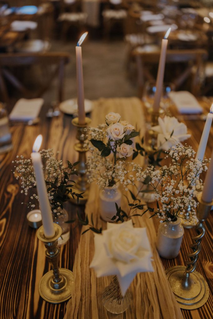 Table set for a formal dinner with tall candles, white roses, and baby's breath on a striped table runner.