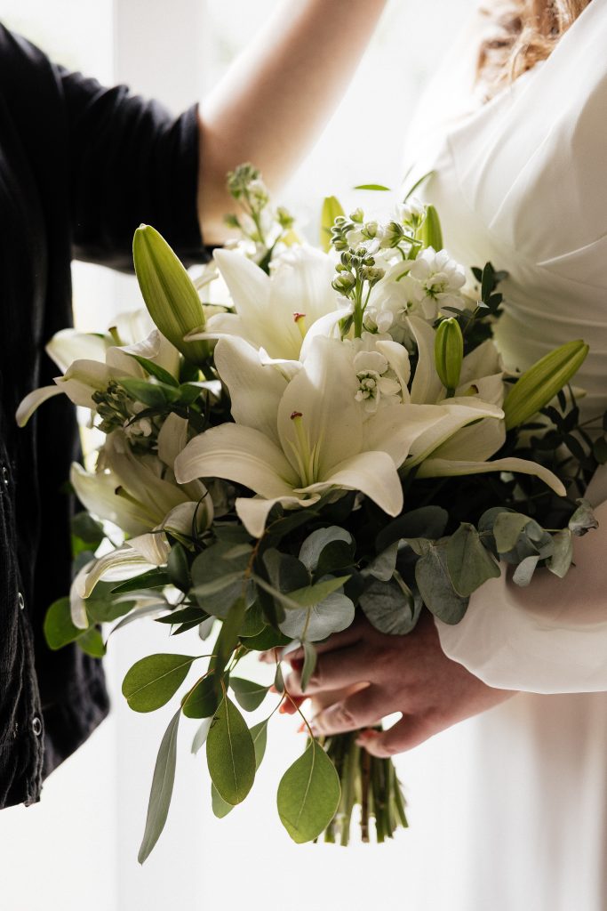 jo paul - fraoch floral design fraoch floral design bride and partner hold a white bouquet of lilies and greenery close together indoors.