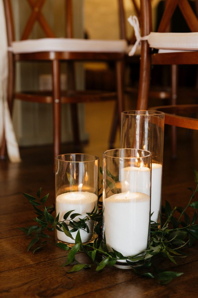 jo paul - fraoch floral design fraoch floral design candle centerpiece with three tall glass hurricane holders and green foliage on a wooden table (warm dining setting).