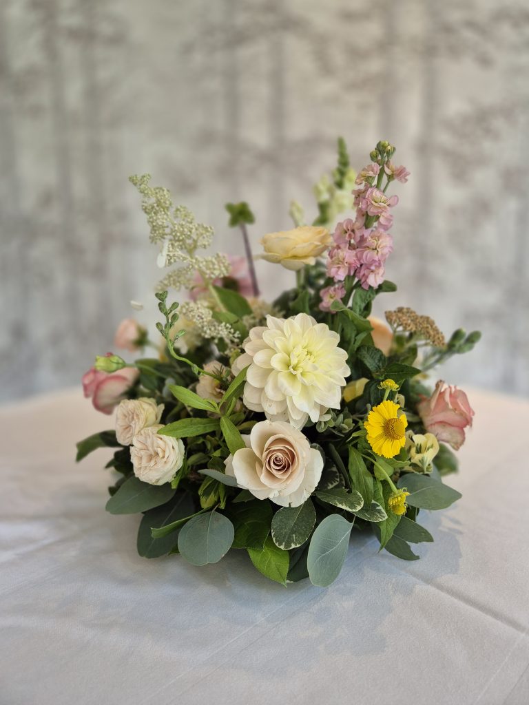 fraoch floral design elegant flower bouquet with cream roses, white dahlias, pink stock, and yellow accents on a pale-gray tablecloth