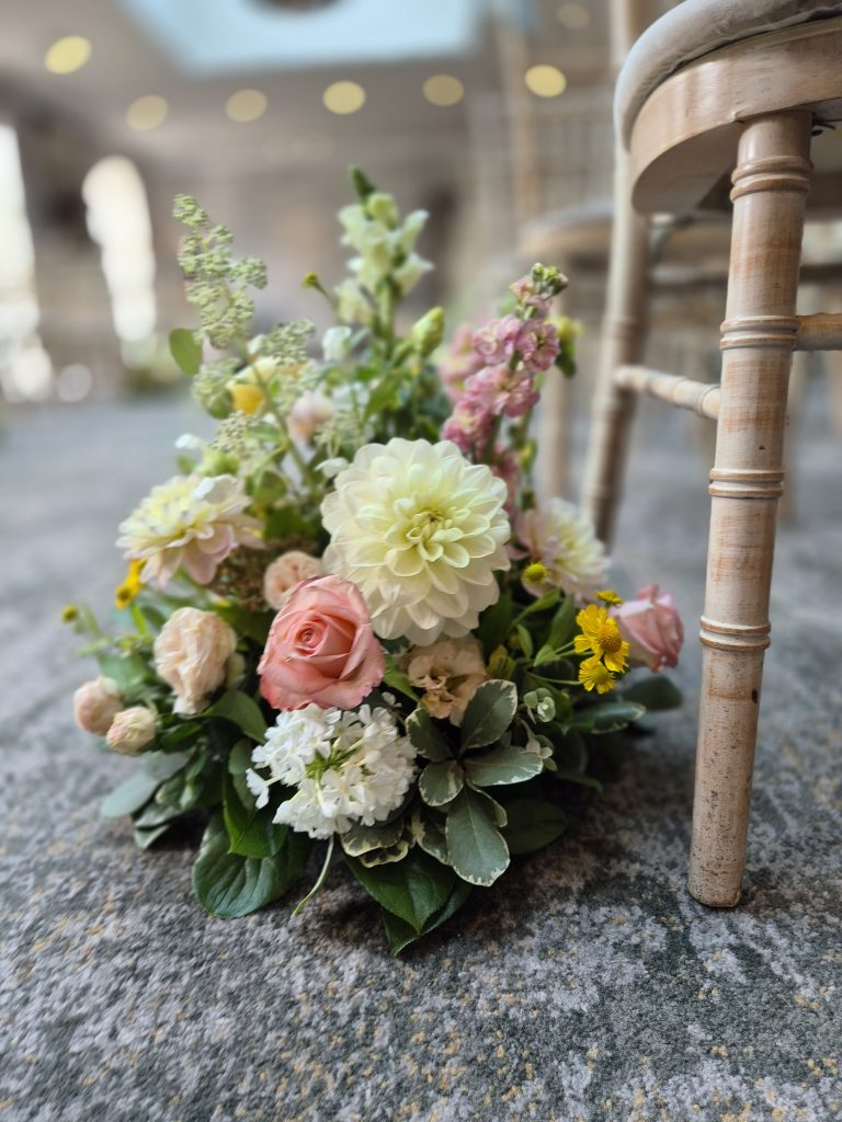 fraoch floral design pastel bouquet of roses, dahlias and greenery on a stone floor beside a wooden chair leg.