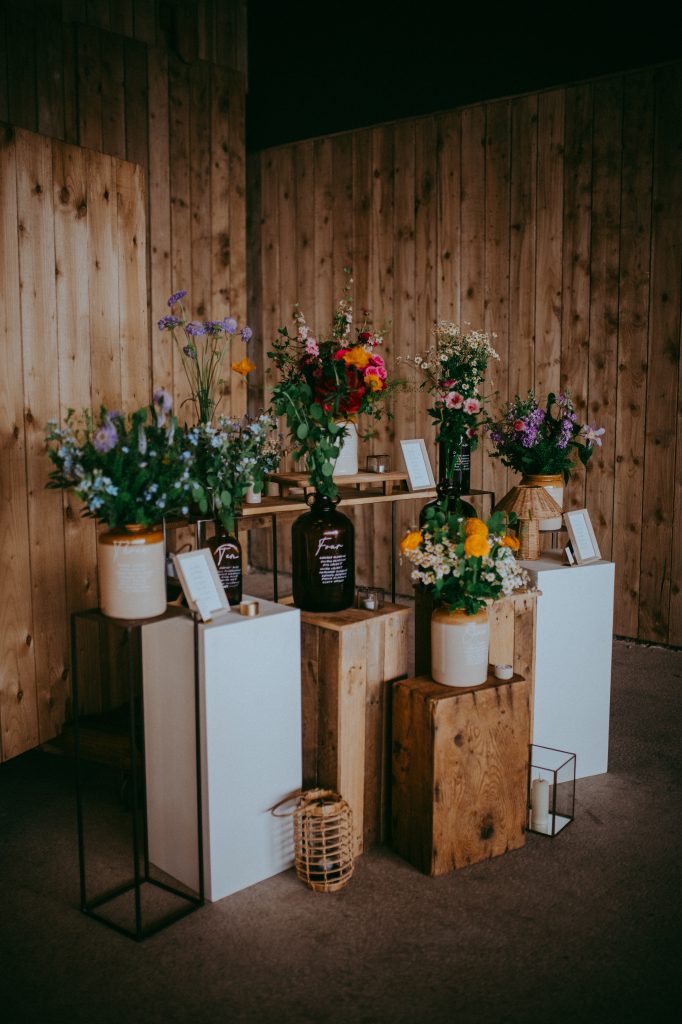 boreland-loch-tay-wedding-fraoch-floral-design 1 - fraoch floral design fraoch floral design arrangements of colorful flowers in vases on rustic wooden pedestals against a wood-paneled wall.