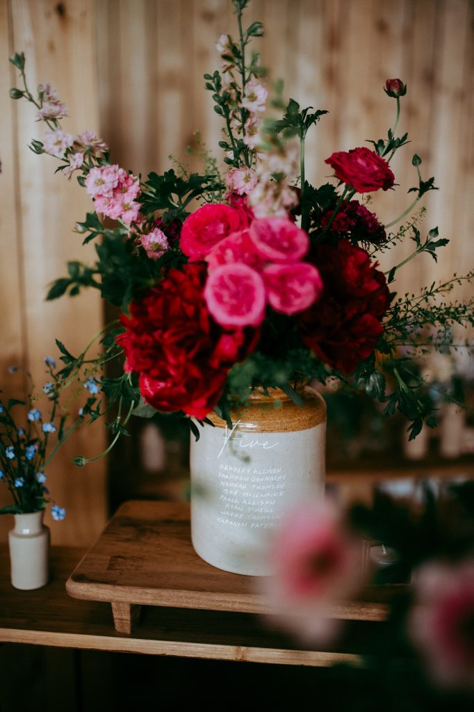 boreland-loch-tay-wedding-fraoch-floral-design 23 - fraoch floral design fraoch floral design bouquet of pink and red flowers in a ceramic vase on a wooden table against a wooden backdrop mend.