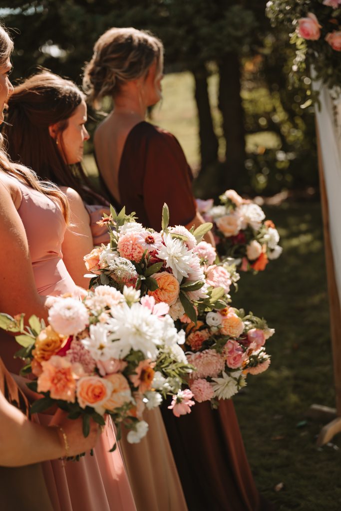 fraoch floral design bridesmaids in pink dresses holding pastel flower bouquets at an outdoor wedding.