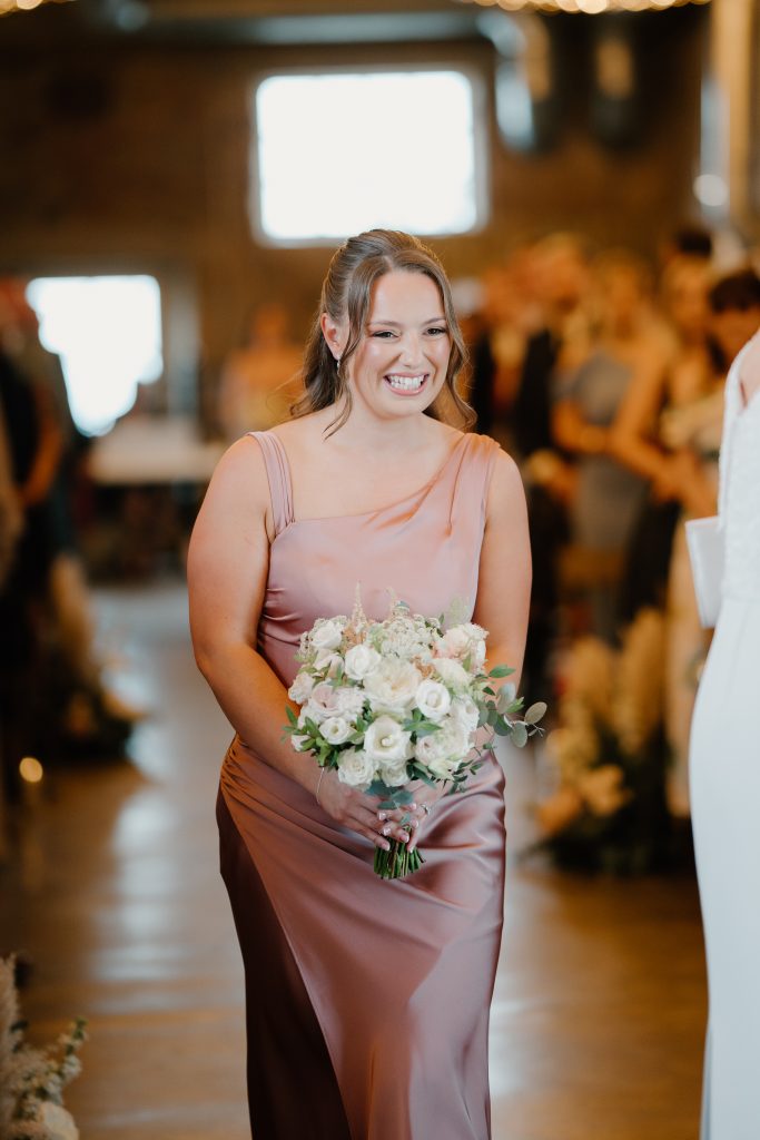fraoch floral design bridesmaid in a blush pink satin dress smiles while holding a white floral bouquet.