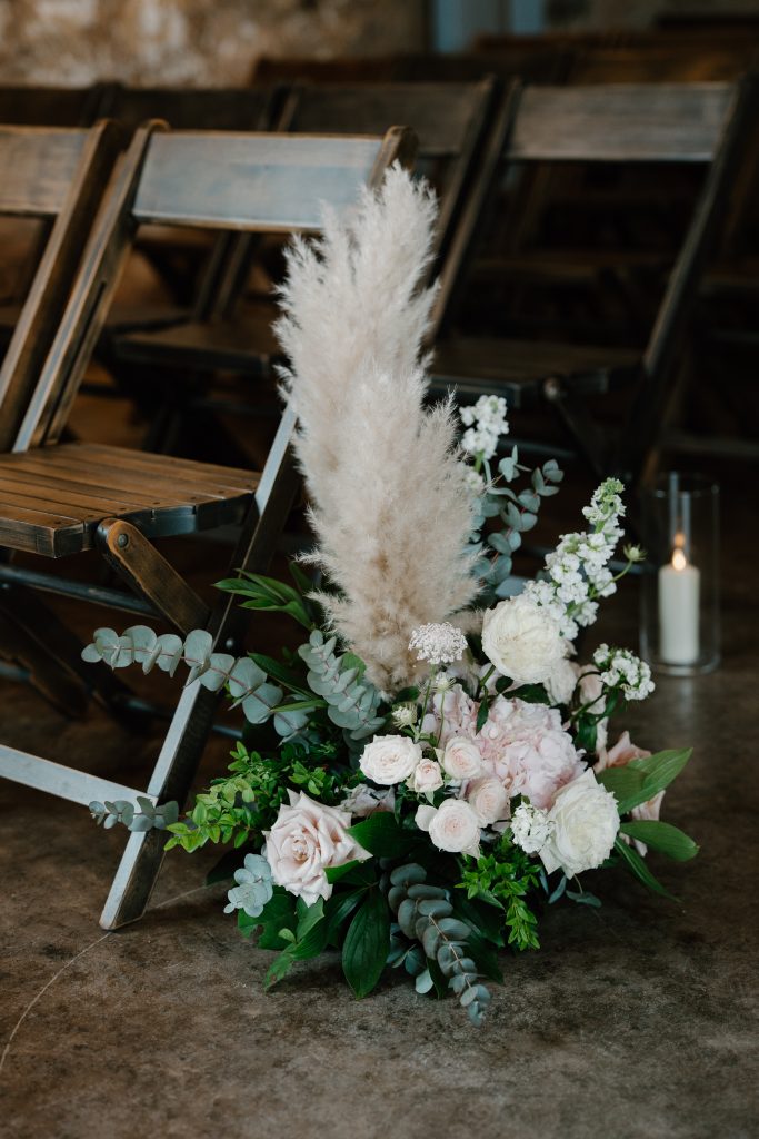 fraoch floral design floral arrangement with pale pink roses, white blossoms and tall pampas grass beside rustic wooden chairs.