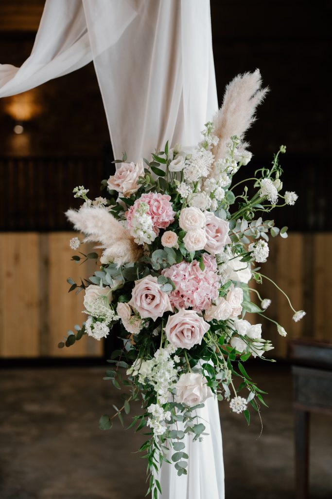 fraoch floral design wedding floral arrangement tied to a white fabric backdrop featuring pink roses, white blooms, and greenery.