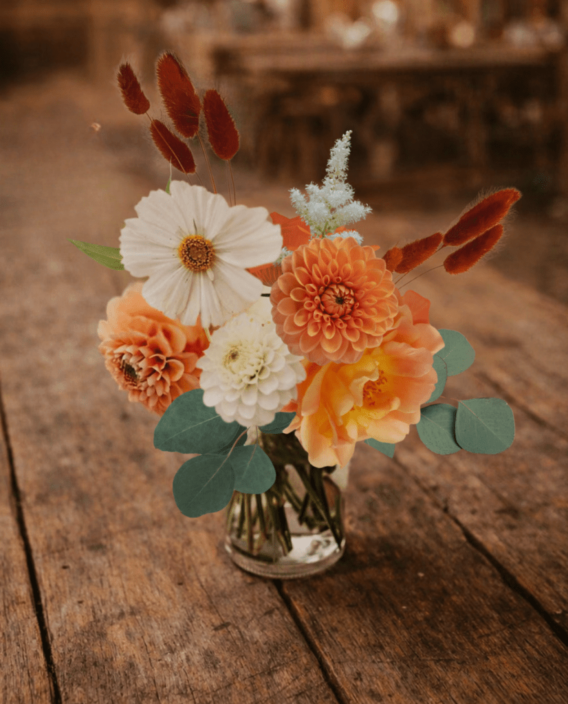 fraoch floral design bouquet of peach and white flowers in a glass vase on a wooden table