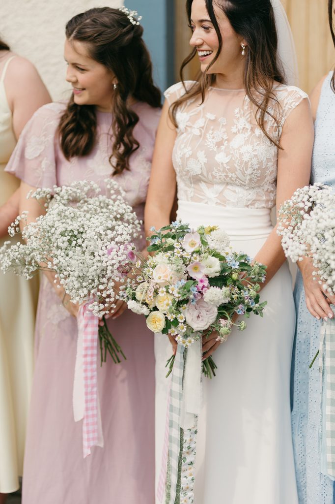 fraoch floral design bridesmaids in pastel dresses holding bouquets of white and pastel flowers, smiling together at a wedding.